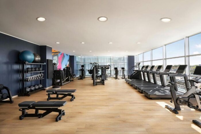 Hotel dentro do Aeroporto de Milão Malpensa 1 Hotel no Aeroporto Malpensa com academia de ginástica: para você se movimentar antes do próximo voo. Essa é a sala com esteiras, pesos e banquinhos para treinar no Sheraton Milan Malpensa