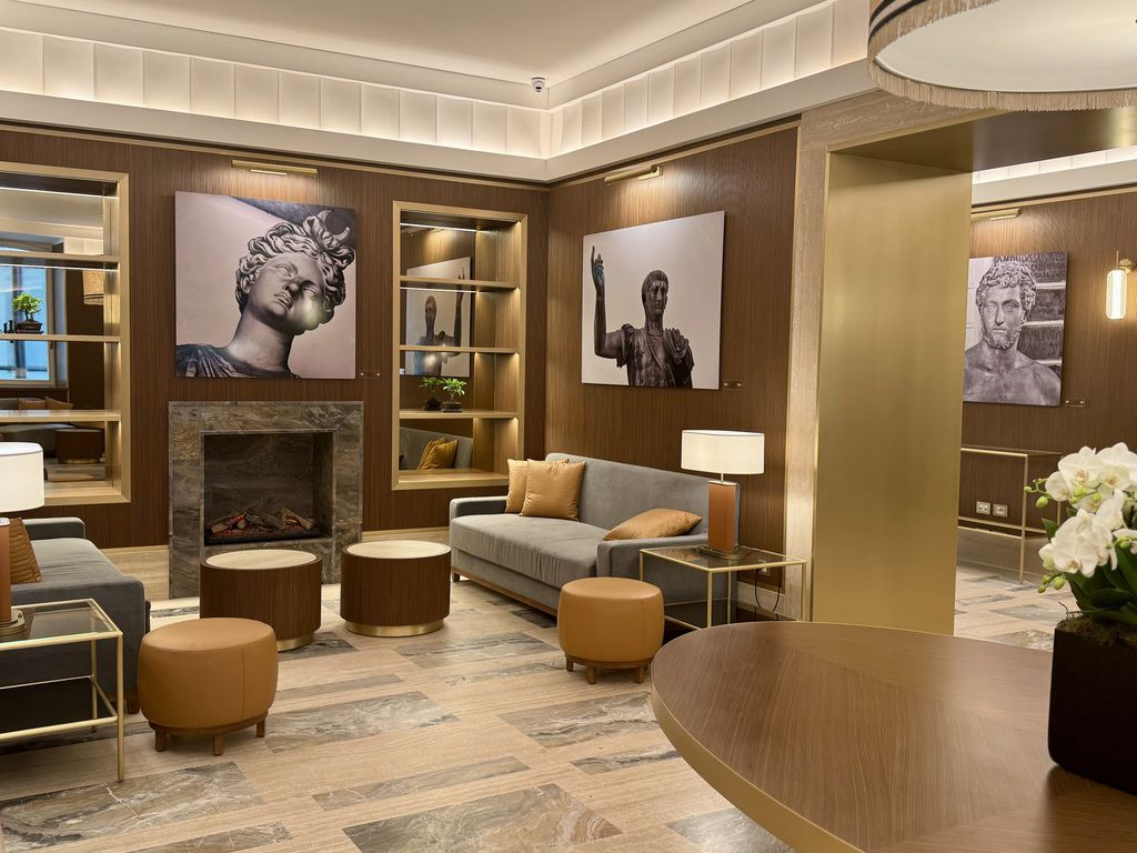 Interior elegante do lounge do Hotel Imperiale em Roma, com sofás modernos, mesas de centro, lareira decorativa e obras de arte inspiradas na Roma Antiga.