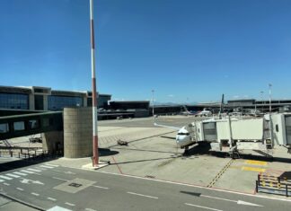 Aeroporto de Milão Malpensa fecha uma pista de março a maio de 2026 - Pátio de estacionamento de aeronaves no Aeroporto de Milão Malpensa com avião comercial conectado ao terminal por ponte de embarque, céu azul ao fundo