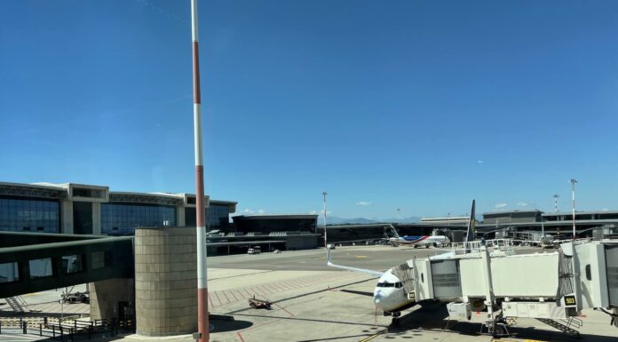 Aeroporto de Milão Malpensa fecha uma pista de março a maio de 2026 - Pátio de estacionamento de aeronaves no Aeroporto de Milão Malpensa com avião comercial conectado ao terminal por ponte de embarque, céu azul ao fundo