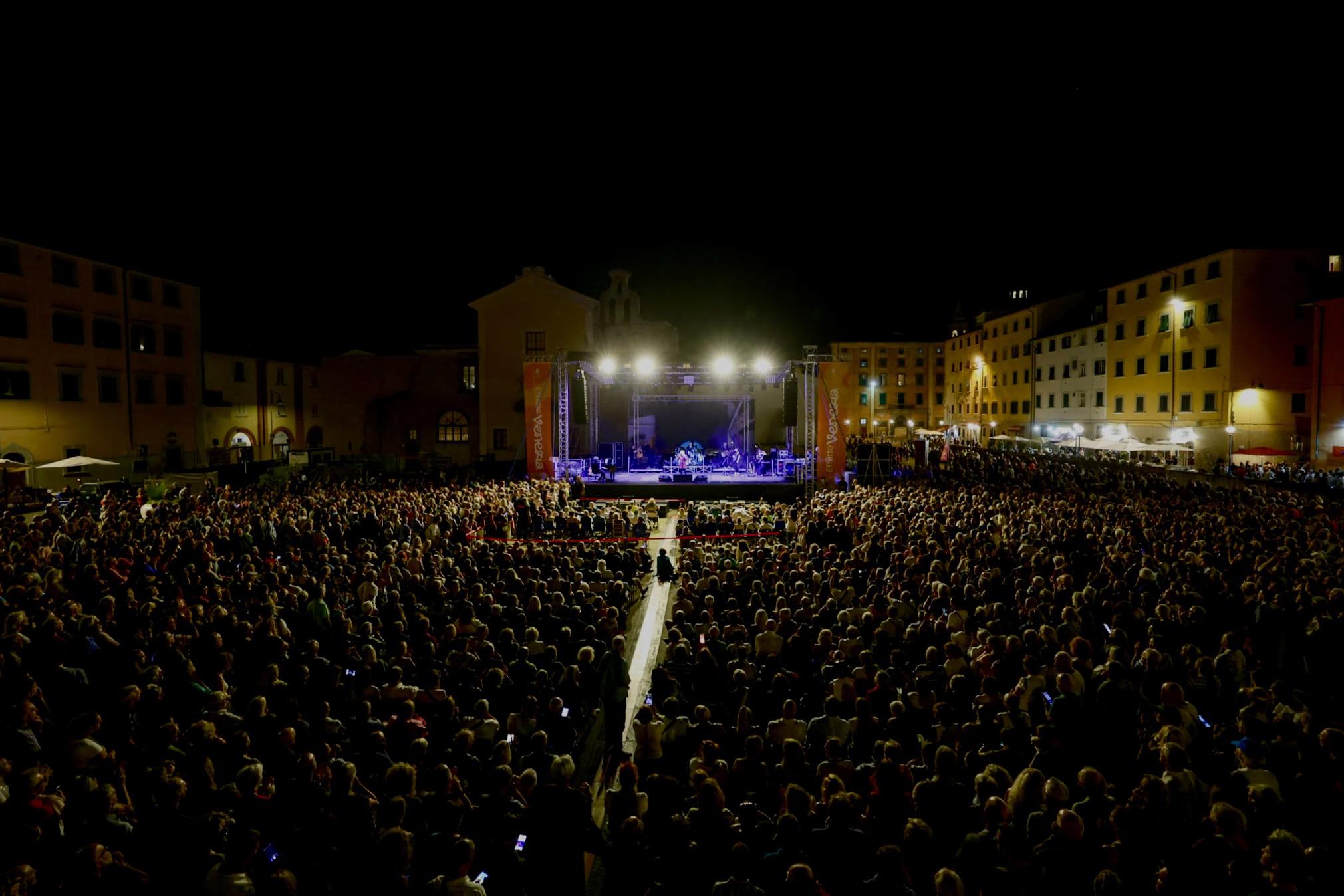 Público acompanha um espetáculo noturno do festival Effetto Venezia em uma praça de Livorno lotada e iluminada no bairro Venezia Nuova