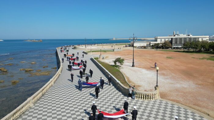 Participantes de um cortejo da Settimana Velica caminham pelo calçadão à beira-mar de Livorno carregando bandeiras