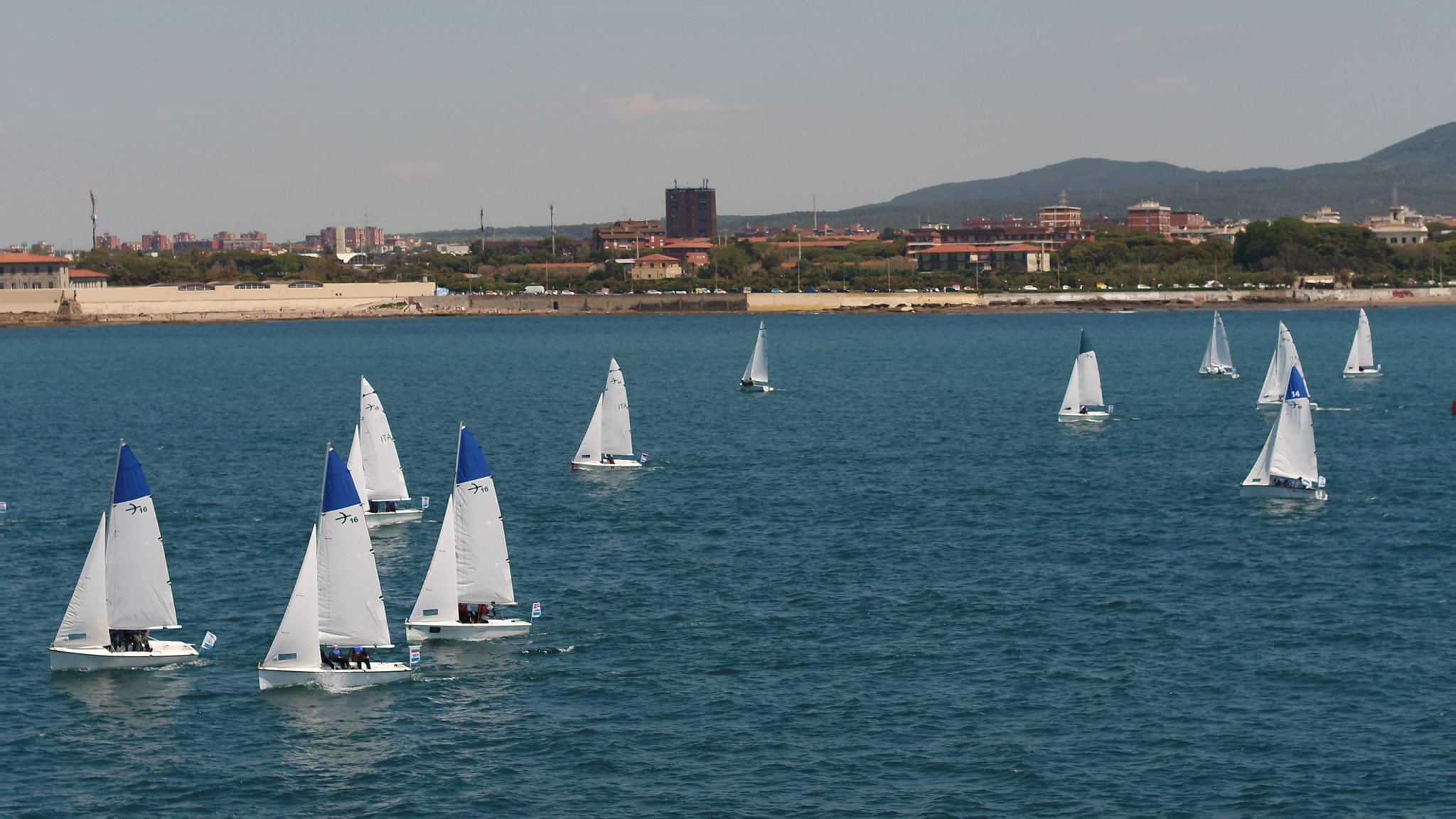 Barcos à vela no mar de Livorno durante a Settimana Velica Internazionale, com a costa da cidade ao fundo