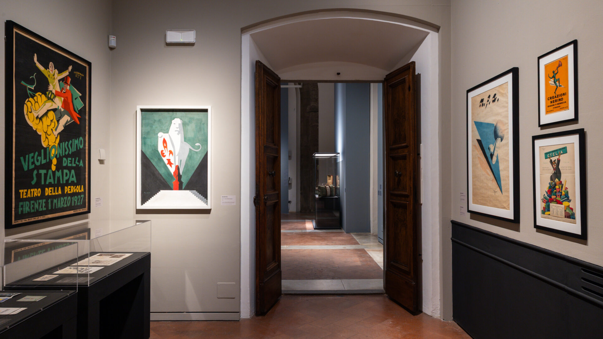 Firenze Déco no Palazzo Medici Riccardi: uma viagem pela elegância dos anos 1920 4 Sala da exposição Firenze Déco no Palazzo Medici Riccardi, com cartazes emoldurados e vitrines em Florença