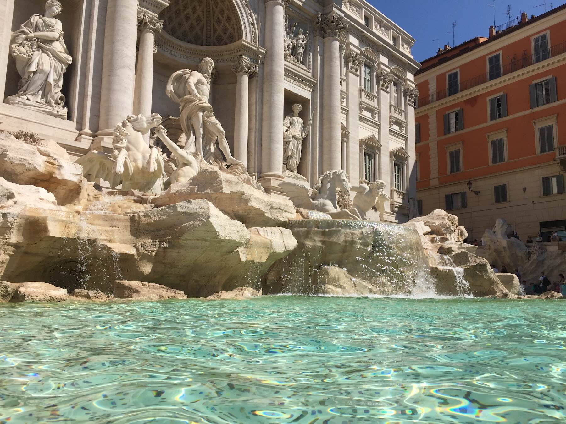 Roma no verão: cuidados para montar um roteiro sem cair em roubadas 3 Fontana di Trevi em Roma, com esculturas barrocas, água cristalina e fachada monumental ao fundo em um dia de sol.