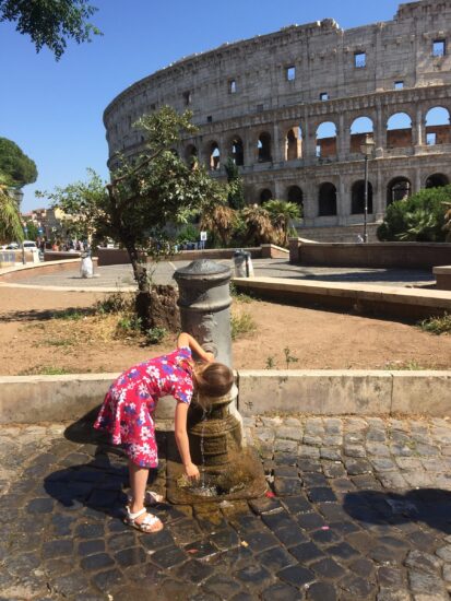 Roma no verão: cuidados para montar um roteiro sem cair em roubadas 2 Criança se refresca em um nasone, uma das tradicionais fontes públicas de água potável de Roma, com o Coliseu ao fundo