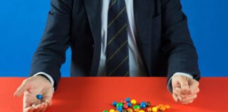 Homem de terno numa mesa vermelha separa confeitos coloridos, obra de Adelita Husni Bey para a Giornata del Contemporaneo 2026