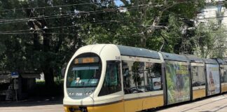 Bonde amarelo e branco da ATM na linha 15 circulando em uma praça arborizada de Milão