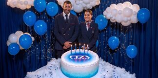 Dois tripulantes da ITA Airways ao lado de um bolo com o logo da companhia e cinco velas