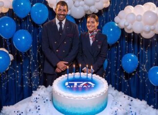 Dois tripulantes da ITA Airways ao lado de um bolo com o logo da companhia e cinco velas